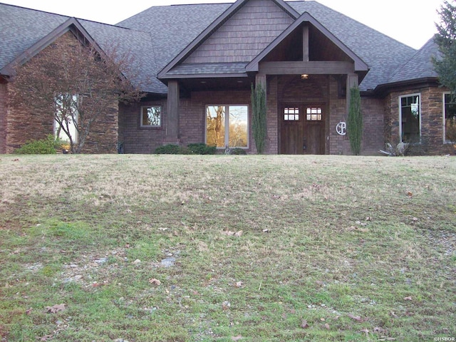 view of front of property featuring brick siding, a front lawn, and roof with shingles