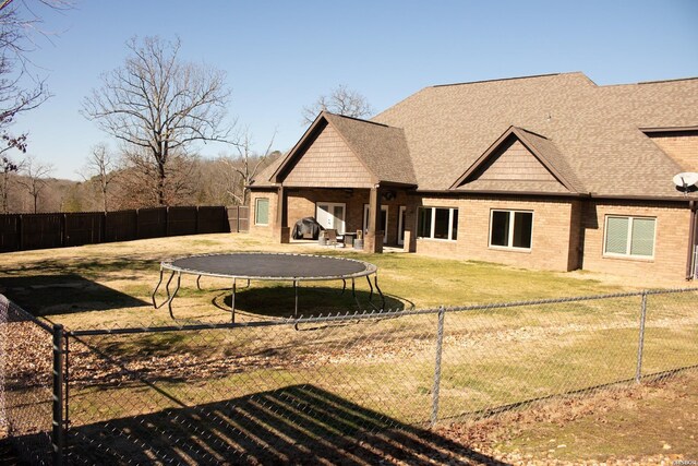 rear view of property with a fenced backyard, a trampoline, and a yard