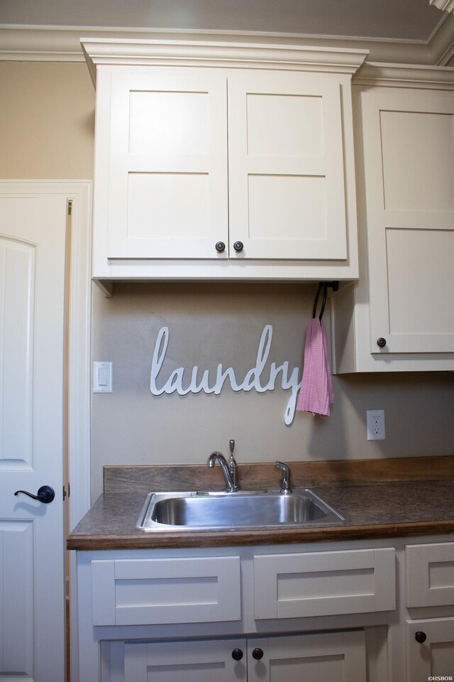 kitchen featuring crown molding, dark countertops, white cabinets, and a sink