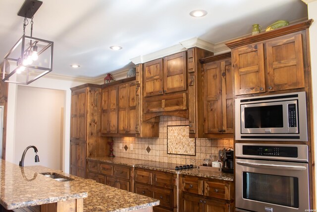 kitchen with decorative light fixtures, a center island with sink, stainless steel appliances, tasteful backsplash, and a sink