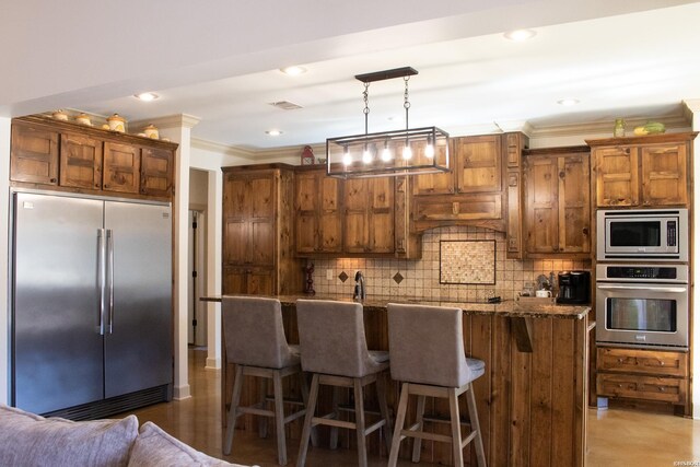 kitchen with built in appliances, light stone counters, a kitchen breakfast bar, decorative backsplash, and pendant lighting