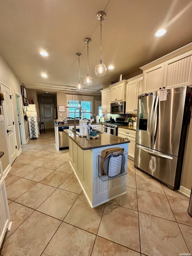 kitchen featuring pendant lighting, stainless steel appliances, dark stone countertops, an island with sink, and a kitchen breakfast bar