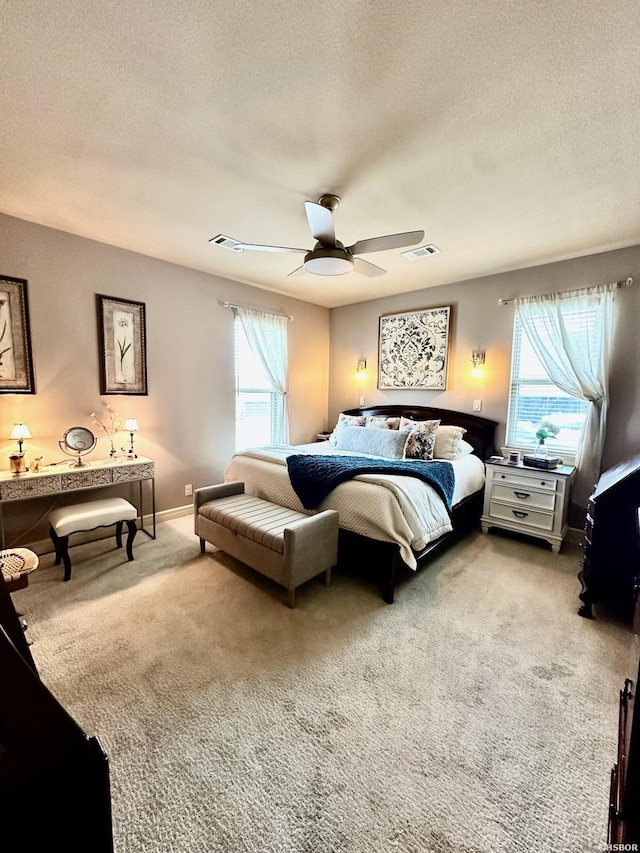 bedroom with a textured ceiling, ceiling fan, visible vents, and light colored carpet