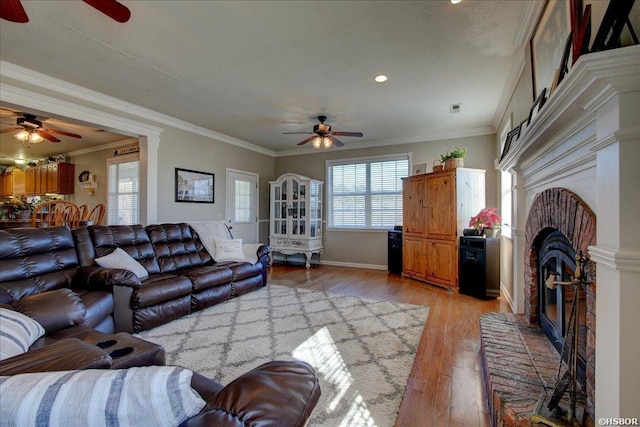 living area featuring ceiling fan, light wood finished floors, a brick fireplace, and crown molding