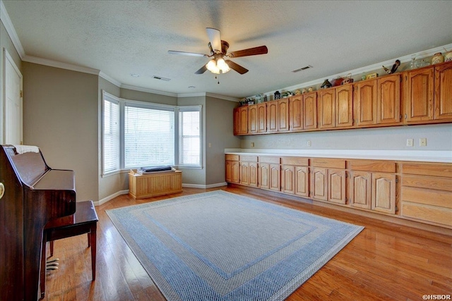 kitchen with light wood-style floors, light countertops, ornamental molding, and visible vents