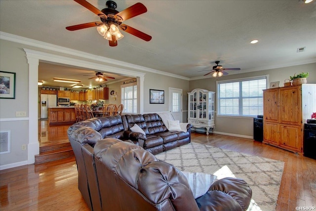 living room featuring baseboards, light wood finished floors, visible vents, and crown molding