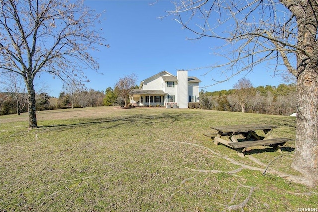 back of property with covered porch, a yard, and a chimney