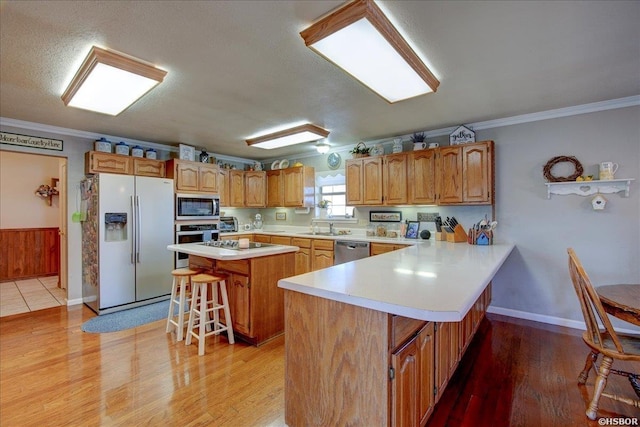 kitchen featuring a kitchen island, a kitchen breakfast bar, light countertops, appliances with stainless steel finishes, and brown cabinets