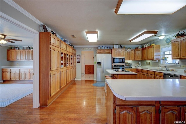 kitchen featuring stainless steel appliances, light countertops, a center island, light wood finished floors, and crown molding