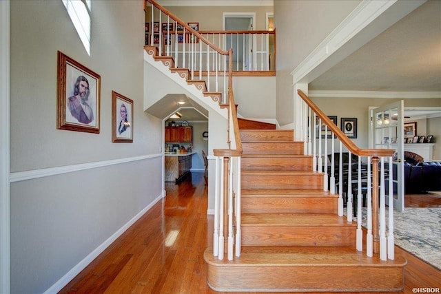 staircase featuring crown molding, a high ceiling, baseboards, and wood finished floors