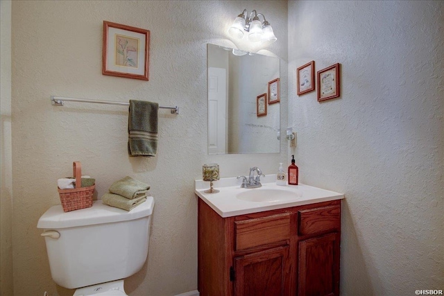 half bath with toilet, a textured wall, and vanity