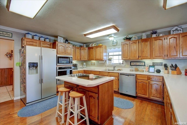 kitchen with light countertops, appliances with stainless steel finishes, ornamental molding, a kitchen island, and a sink