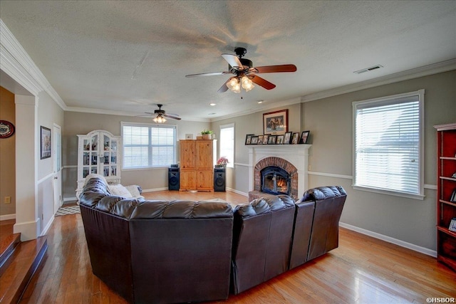 living area with light wood-style floors, visible vents, a fireplace, and ornamental molding