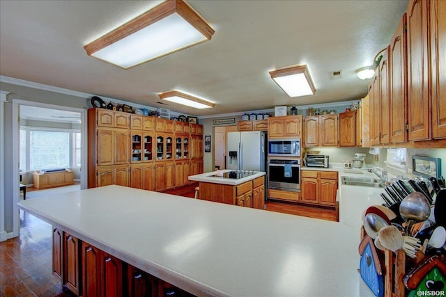 kitchen with a kitchen island, stainless steel appliances, crown molding, light countertops, and a sink