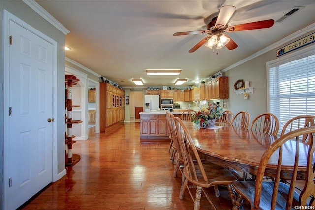 dining room featuring ceiling fan, light wood-type flooring, visible vents, and crown molding