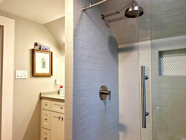 full bath featuring a textured wall, vaulted ceiling, a tile shower, and vanity