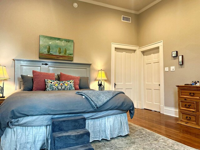 bedroom with baseboards, visible vents, a towering ceiling, wood finished floors, and crown molding