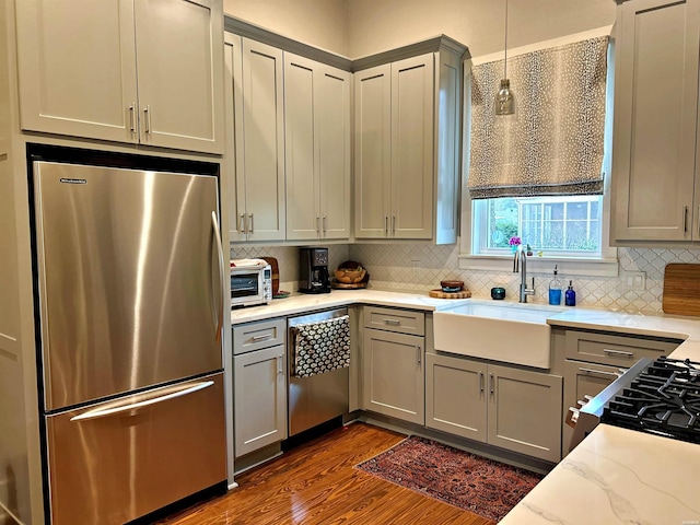 kitchen with gray cabinetry, a sink, appliances with stainless steel finishes, dark wood-style floors, and decorative light fixtures