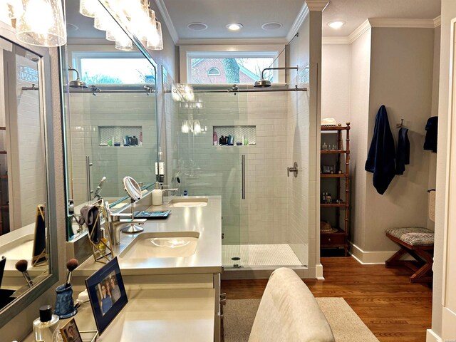 bathroom featuring crown molding, double vanity, a sink, a shower stall, and wood finished floors