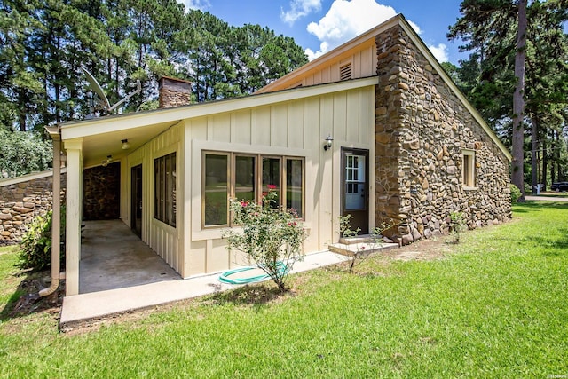 rear view of property featuring stone siding, board and batten siding, a chimney, and a yard
