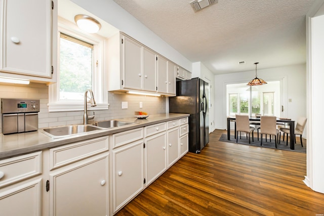 kitchen featuring visible vents, black fridge, dark wood-style floors, white cabinetry, and a sink