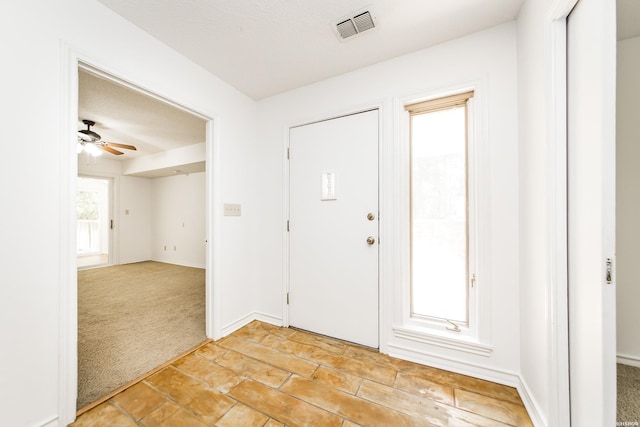 entrance foyer with a ceiling fan, light colored carpet, visible vents, and baseboards