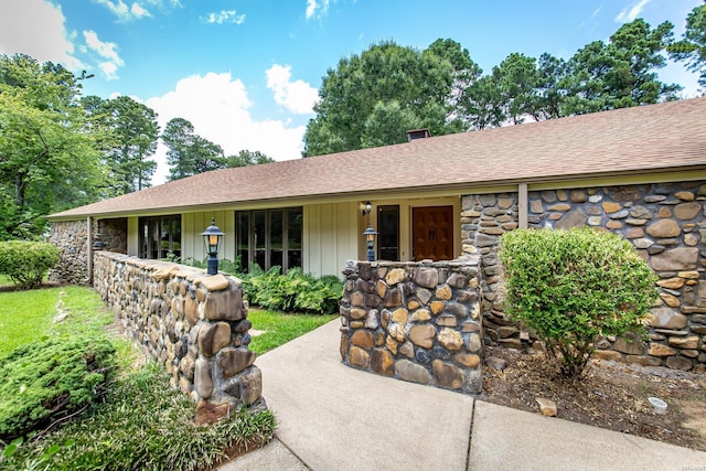 ranch-style house with board and batten siding, stone siding, roof with shingles, and a chimney