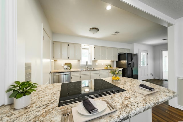 kitchen with a sink, stainless steel dishwasher, backsplash, stovetop, and black refrigerator with ice dispenser