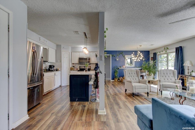living area featuring wood finished floors, a textured ceiling, visible vents, an inviting chandelier, and baseboards