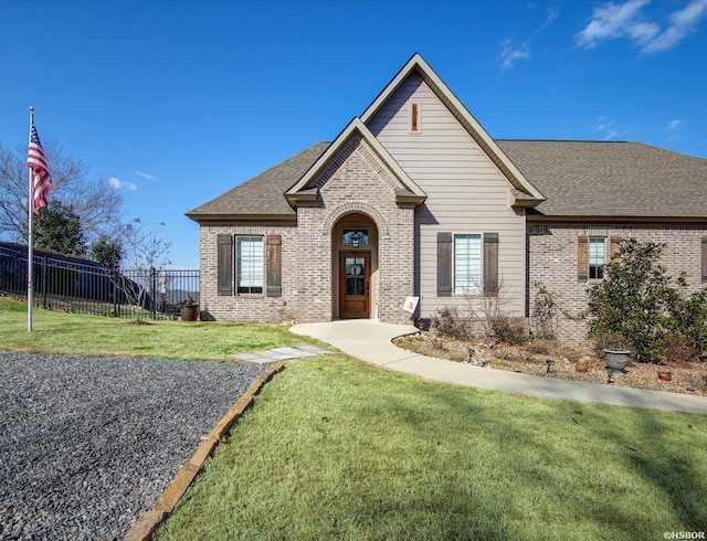 view of front of property featuring a shingled roof, a front yard, brick siding, and fence