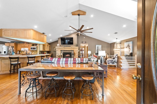 kitchen featuring a fireplace, stainless steel refrigerator with ice dispenser, a breakfast bar area, light wood-style flooring, and open floor plan