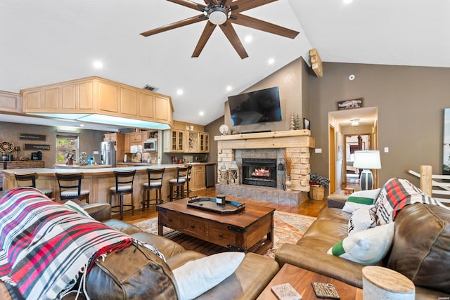 living area with visible vents, ceiling fan, a stone fireplace, and light wood finished floors