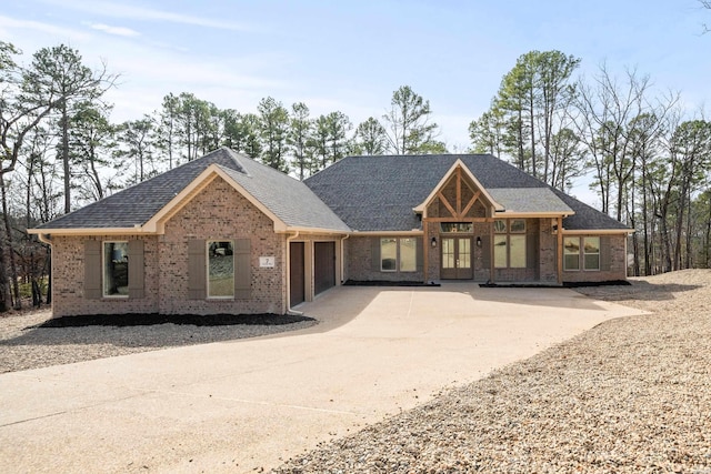 view of front facade with a garage, driveway, a shingled roof, and brick siding