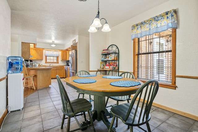 dining room featuring light tile patterned floors, a textured ceiling, a chandelier, and baseboards