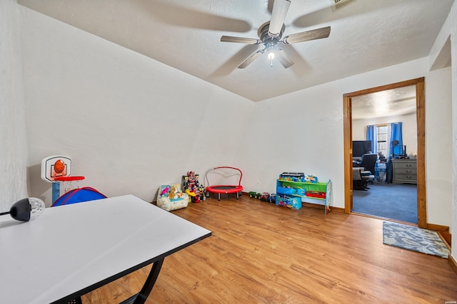 playroom with a textured ceiling, ceiling fan, light wood-style flooring, and baseboards