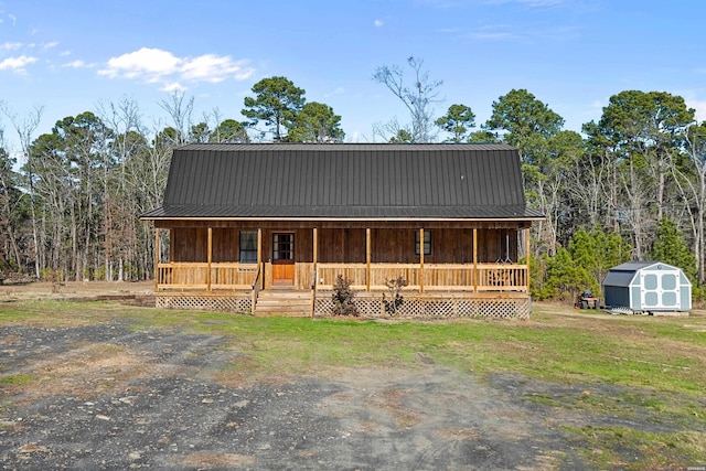 view of front of house featuring an outbuilding, covered porch, a storage shed, metal roof, and a front lawn