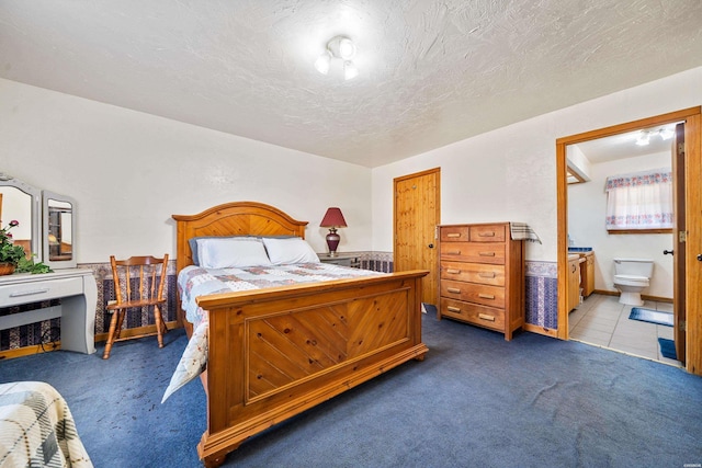 bedroom featuring a textured ceiling, dark tile patterned floors, dark carpet, and ensuite bath