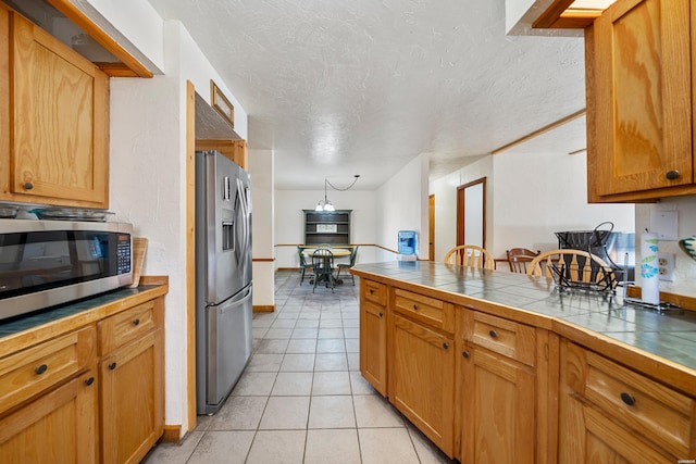 kitchen with tile countertops, light tile patterned floors, a textured ceiling, stainless steel appliances, and brown cabinets