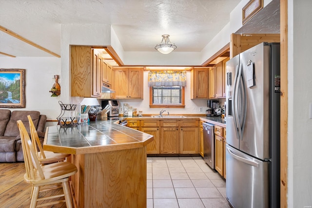 kitchen with brown cabinets, stainless steel appliances, dark countertops, a sink, and a peninsula