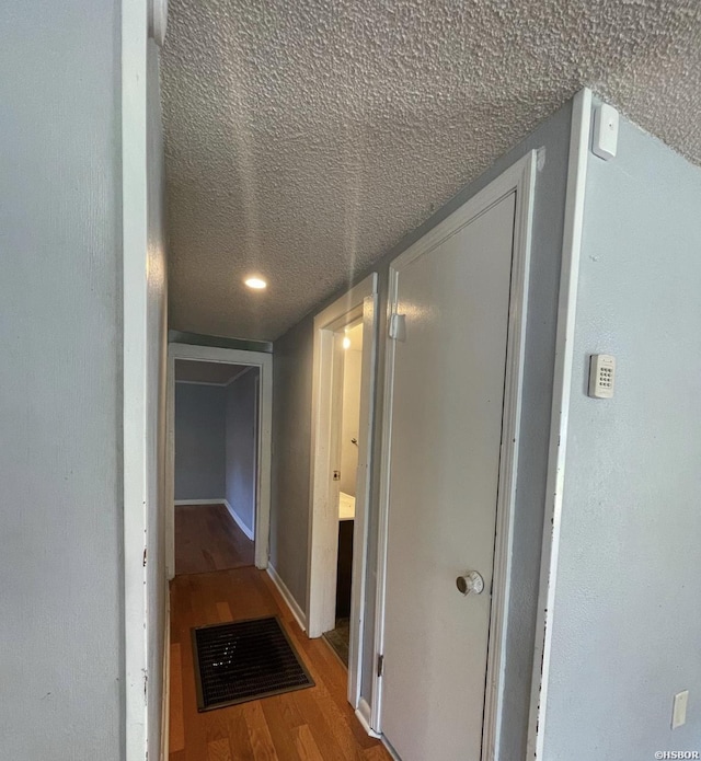 hallway featuring a textured ceiling, wood finished floors, and visible vents