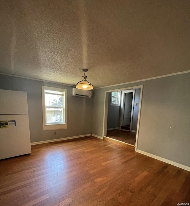 unfurnished dining area with crown molding, baseboards, wood finished floors, and a wall mounted air conditioner