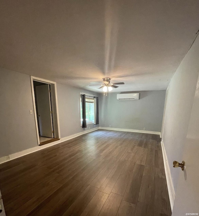 spare room with dark wood-style floors, an AC wall unit, ceiling fan, and baseboards