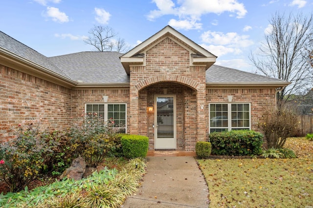 entrance to property with a yard, brick siding, and a shingled roof