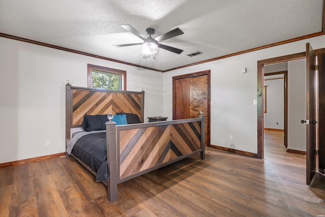 bedroom featuring a textured ceiling, wood finished floors, visible vents, and ornamental molding