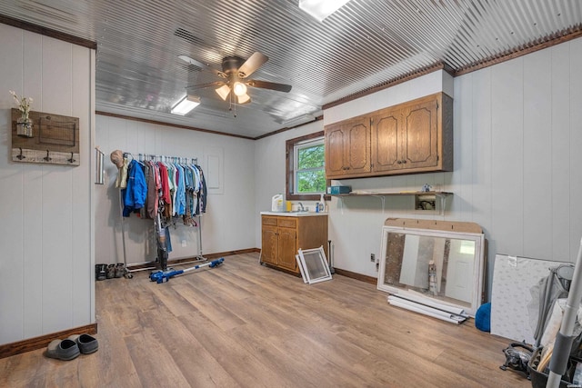 laundry room with light wood finished floors, a sink, ceiling fan, cabinet space, and ornamental molding