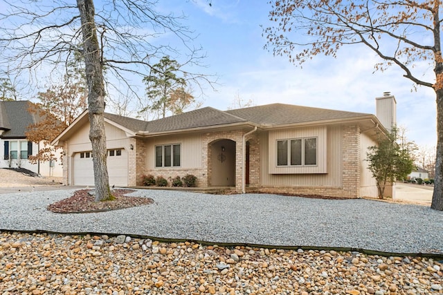 ranch-style house featuring driveway, a shingled roof, a chimney, an attached garage, and brick siding