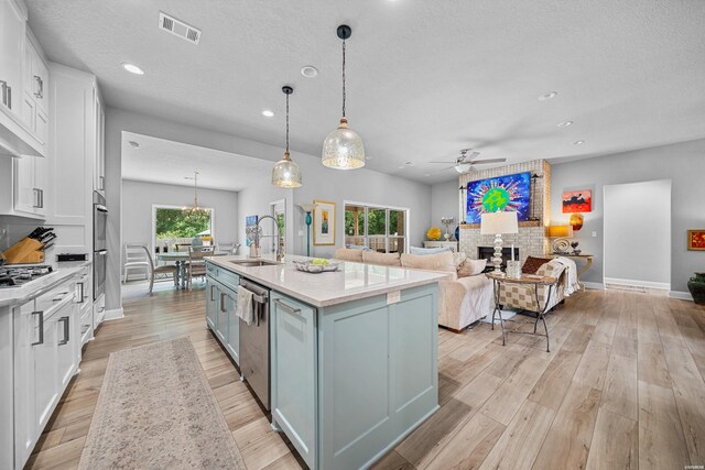 kitchen with visible vents, white cabinets, a kitchen island with sink, pendant lighting, and a sink