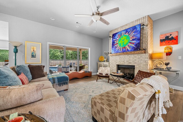 living area featuring visible vents, a brick fireplace, ceiling fan, wood finished floors, and baseboards