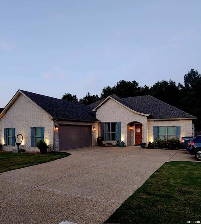 ranch-style house with a garage, a front yard, roof with shingles, and driveway