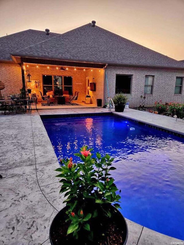 pool at dusk with a patio area and an outdoor pool